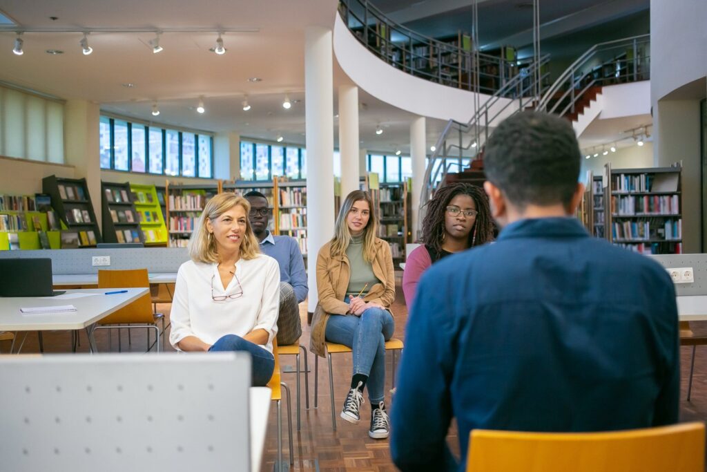 Seminar in moderner Bibliothek: Gruppe von Erwachsenen hört aufmerksam einem Vortragenden bei einer Weiterbildung oder Schulung zu